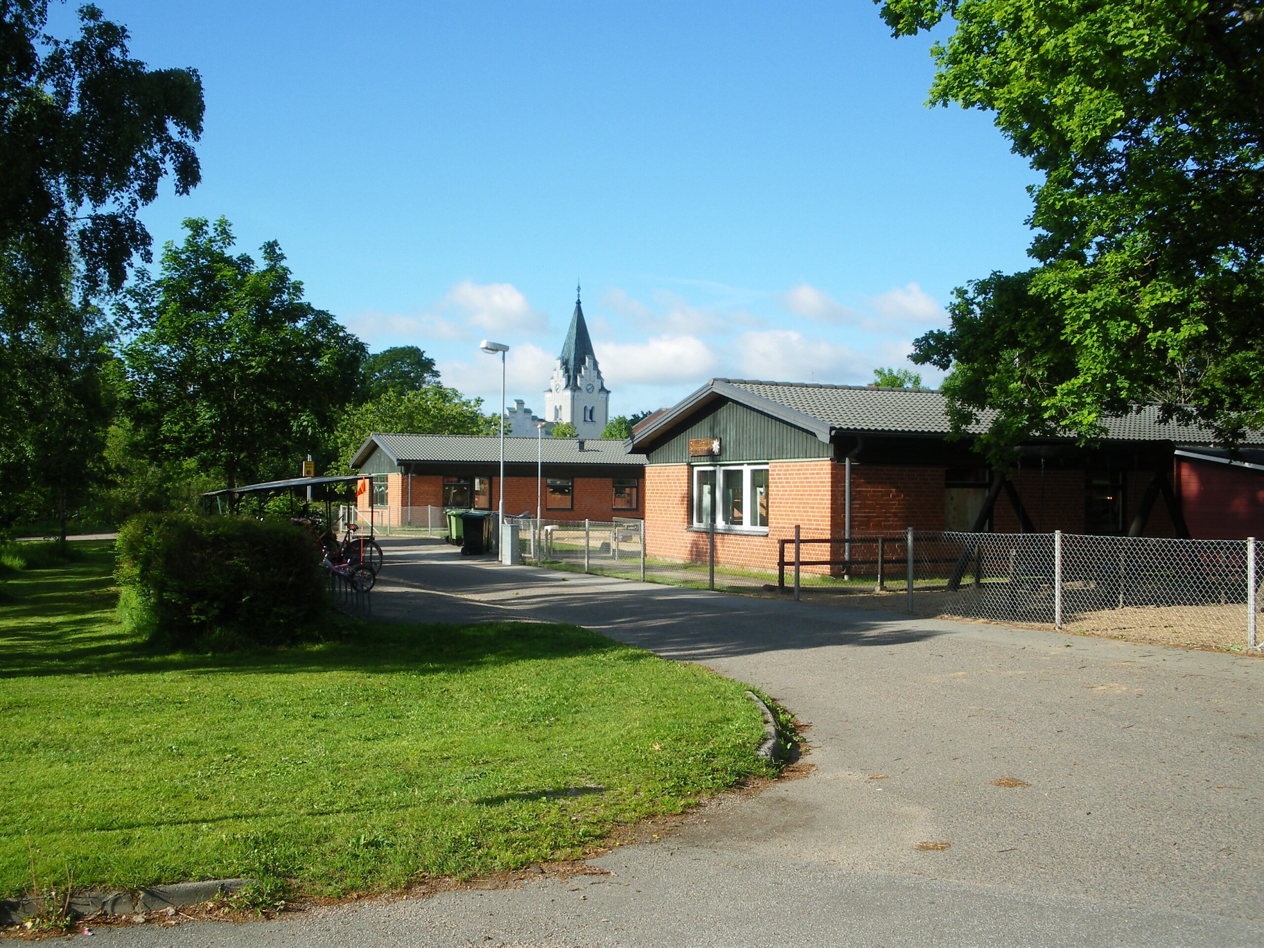 Bild på en förskola vid en cykelväg och ett grönområde. Höörs Kyrka i bakgrunden.